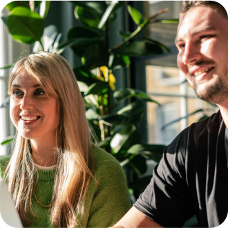 Two colleagues smiling in front of plant